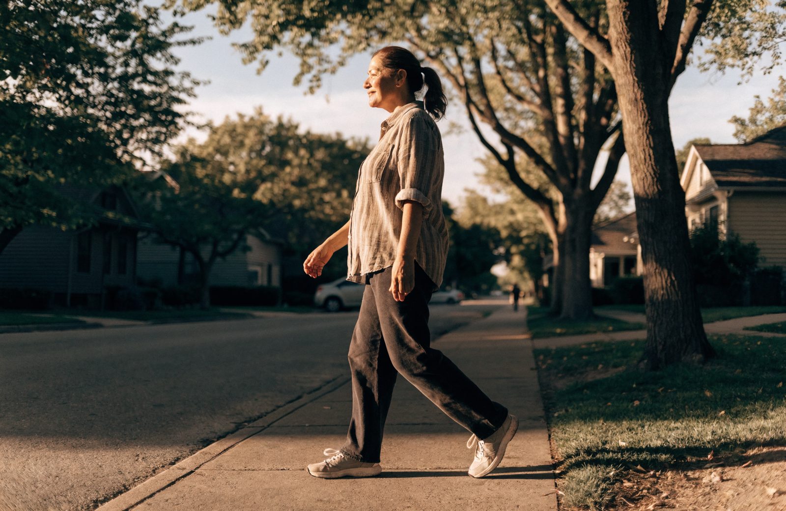 A woman walking outside on a sunny neighborhood sidewalk, relaxed and at ease